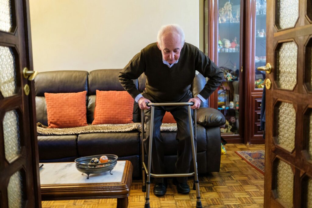 Senior man using walker to stand up from sofa in living room